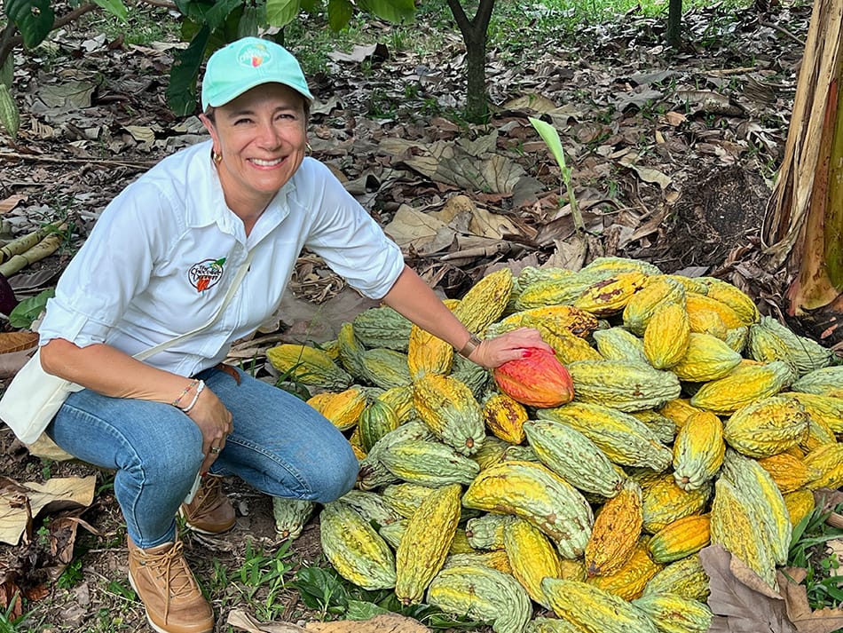 Image shows Julia Ocampo from Luker Chocolate next to a pile of cocoa pods.