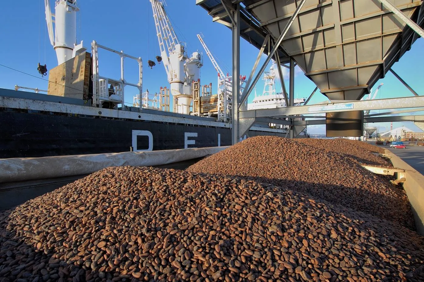 Image shows cocoa beans at a port being loaded onto a boat.