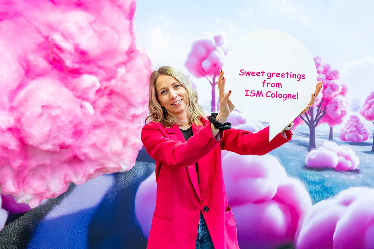 Image shows a woman holding up a sign welcoming visitors to ISM Cologne
